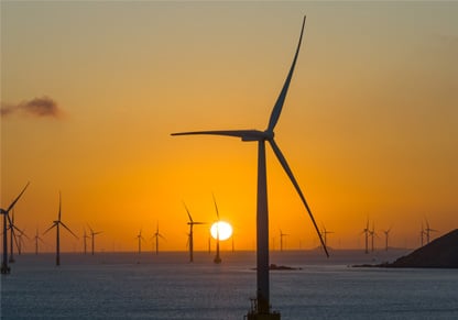 An offshore wind farm backed by an orange sky. 